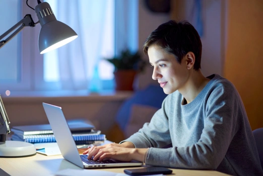 Eine Frau mit kurzen Haaren sitzt konzentriert am Schreibtisch vor ihrem Laptop.
