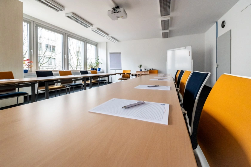 Detailsansicht eines Seminarraums mit Tischen und Stühlen, Flipchart und Tafel.