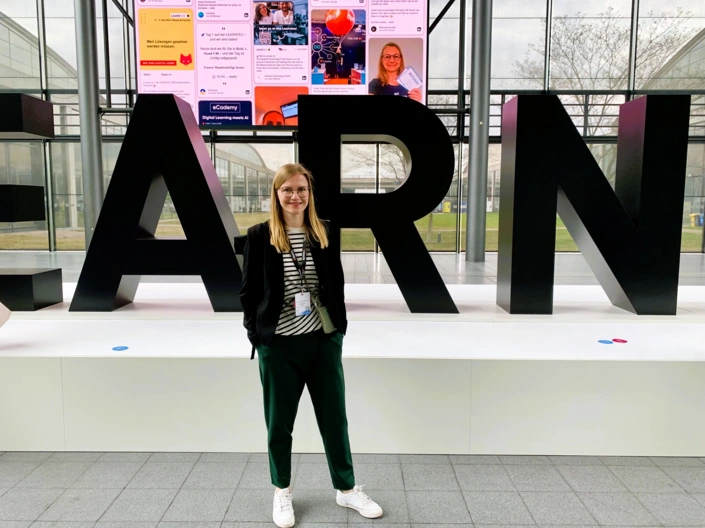 Eine junge Frau steht vor einer Buchstaben-Installation auf der Messe Learntec.
